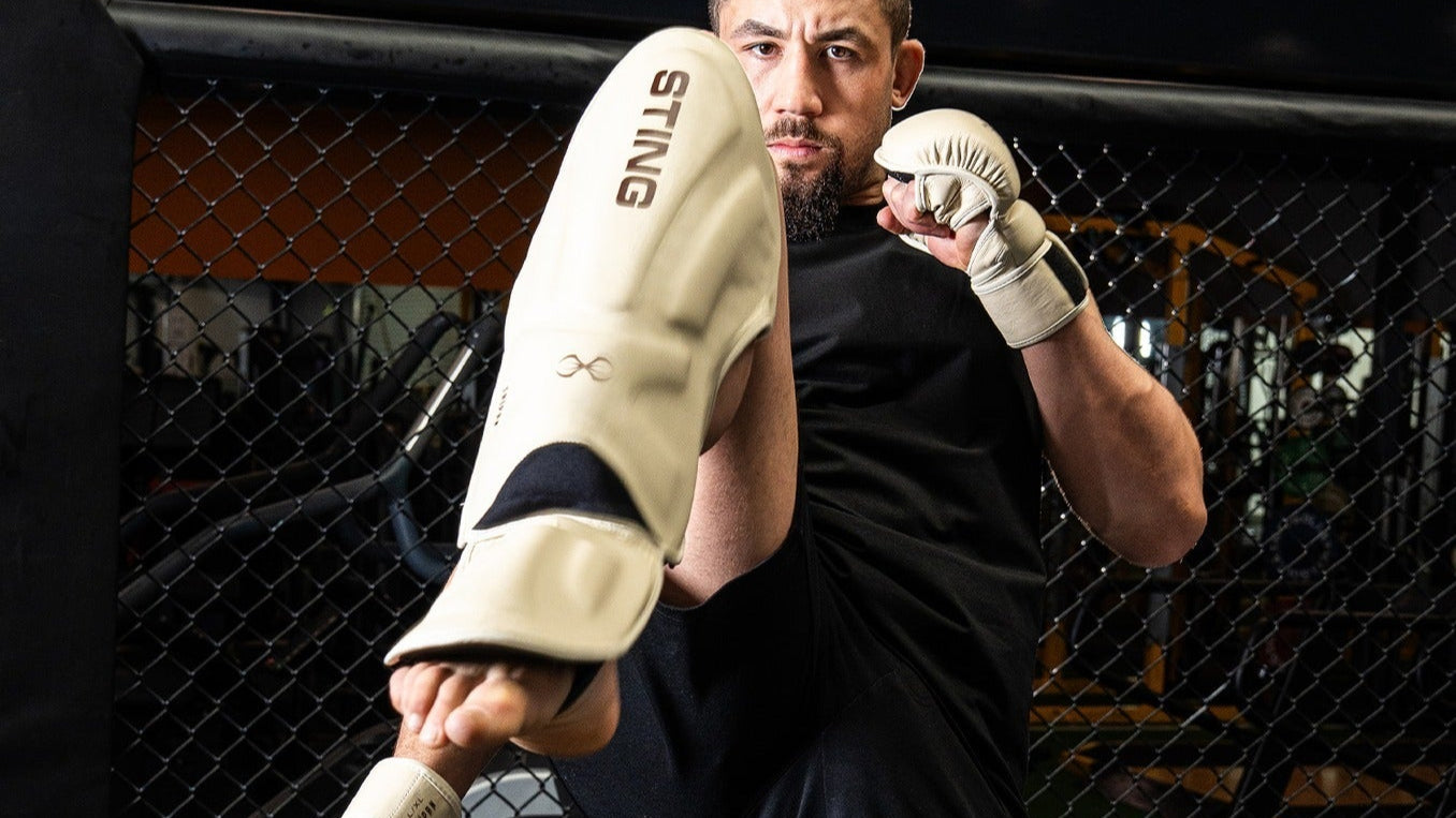 Person in a martial arts stance with gear, standing in front of a cage.