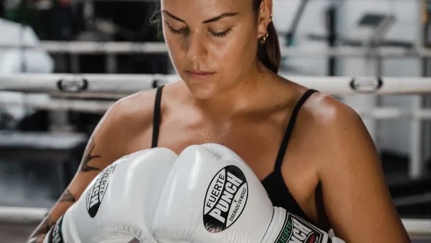 Woman in boxing stance wearing white boxing gloves and shorts with 'Punch' branding in a boxing ring.